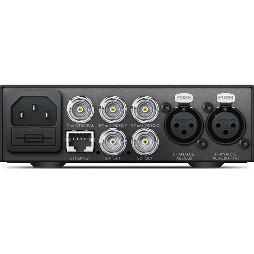 The Blackmagic Design Teranex Mini Analog to SDI 12G Converter is a compact, rectangular device with a matte black finish. The front panel features a USB port and ventilation grilles, while the rear panel includes component, S-Video, and composite analog video inputs, two 12G-SDI outputs, an Ethernet port, and XLR audio inputs. This design facilitates professional video and audio signal conversion in broadcast and post-production environments.