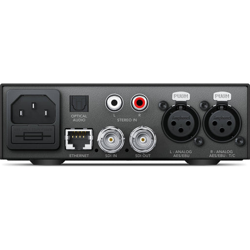 The Blackmagic Design Teranex Mini Audio to SDI 12G Converter is a compact, rectangular device with a matte black finish. The front panel features a USB port and ventilation grilles, while the rear panel includes balanced XLR audio inputs, unbalanced RCA audio inputs, an optical audio input, a 12G-SDI output, an Ethernet port, and a standard IEC power input. This design facilitates professional audio embedding into SDI signals in broadcast and post-production environments.