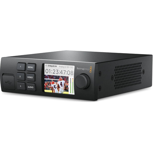 The Blackmagic Design Teranex Mini SDI to HDMI 8K HDR Converter is a compact, rectangular device with a matte black finish. The front panel features a color LCD screen, control buttons, and a rotary knob for easy navigation and monitoring. The rear panel includes four 12G-SDI inputs, four HDMI 2.0 outputs, analog audio outputs, a USB Type-C port, and an Ethernet port. This design facilitates the conversion of SDI sources to HDMI in various formats, including HD, Ultra HD, and 8K.